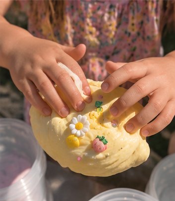 Hands squishing yellow butter slime topped with a daisy and strawberry charm